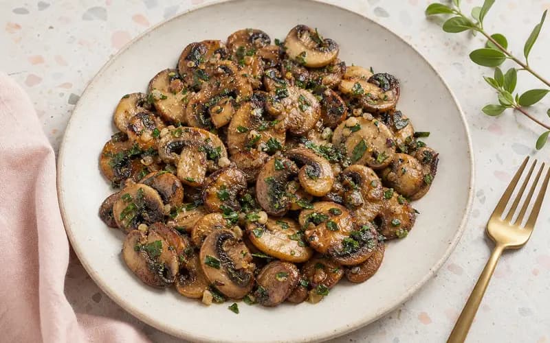 Poêlée de champignons à l'ail et au persil dorés dans une assiette rustique, persil frais ciselé par-dessus