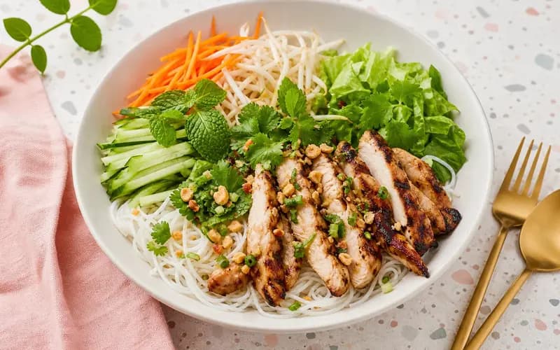 Bo bun léger au poulet, vermicelles de riz, crudités croquantes, menthe et cacahuètes dans un grand bol blanc